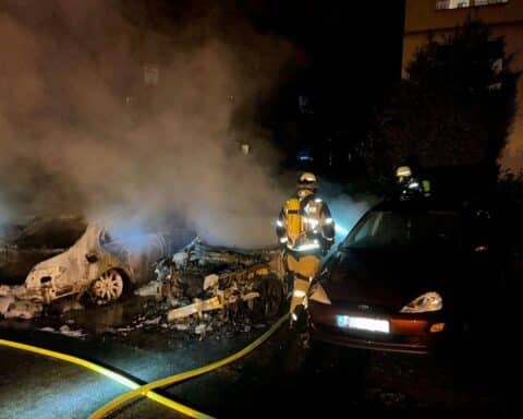 Brandstelle mit zwei ausgebrannten Autos, Feuerwehr im Einsatz zur Brandbekämpfung und Abdämmung.