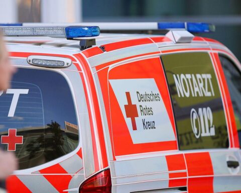 Ein verletzter E-Scooter-Fahrer wird von Rettungskräften versorgt, Unfallstelle im Hintergrund.