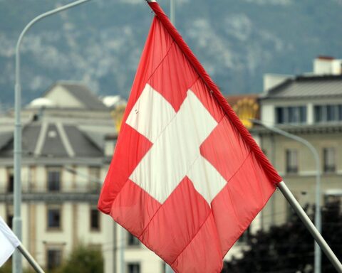 Fahne der Schweiz vor urbanem Hintergrund, symbolisiert Offenheit und globale Vernetzung in der Wirtschaft.