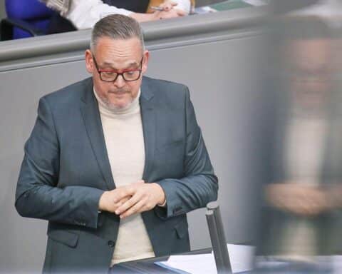 Martin Reichardt im Gespräch über umstrittene Geste, umgeben von Parteikollegen und einem knienden Mann.