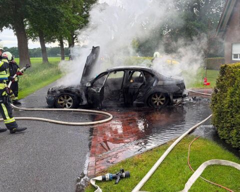 Ausgebranntes Auto auf Hauseinfahrt, Feuerwehr bei Löscharbeiten, Rauch und Einsatzkräfte sichtbar.