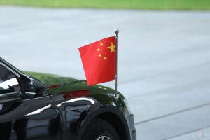 Chinesische Flagge mit Hybridautos im Hintergrund, symbolisiert EU-Zölle und Handelskonflikt.