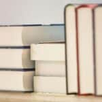 Ein Stapel Bücher auf einem Tisch, daneben ein Stift und Notizpapier für Anträge.