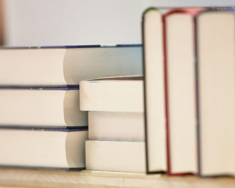 Ein Stapel Bücher auf einem Tisch, daneben ein Stift und Notizpapier für Anträge.