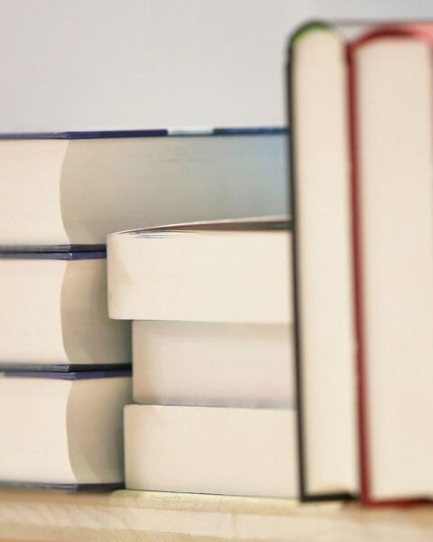 Ein Stapel Bücher auf einem Tisch, daneben ein Stift und Notizpapier für Anträge.