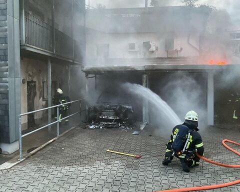 Auto-Brand unter Carport, Feuerwehr im Einsatz, Wohngebäude betroffen, evakuierte Familie, Einsatzkräfte mit Löschfahrzeugen.