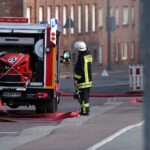 Feuerwehr löscht Brand in Entsorgungsbetrieb, Flammen und Rauch in großer Halle sichtbar.