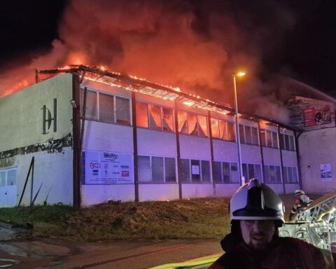 Drehleiter im Einsatz zur Bekämpfung eines Dachstuhlbrands in Industriehalle, Feuerwehrkräfte aktiv.
