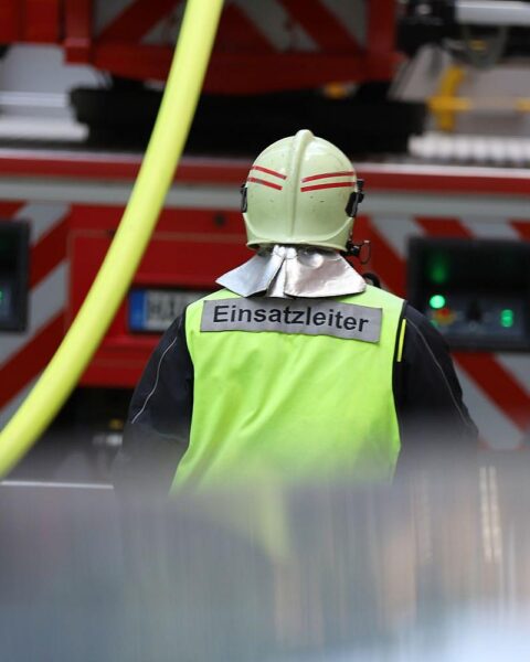 Einsatzleiter und Feuerwehrkräfte bei einem Brand in einem Mehrfamilienhaus, evakuierte Bewohner.