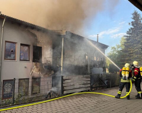Einsatzkräfte löschen ein brennendes Gebäude, Flammen drohen auf angrenzendes Wohnhaus überzugreifen.