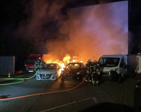 Feuerwehr löscht brennende Pkw und Transporter auf Parkplatz, Gefahr von Brandausbreitung.