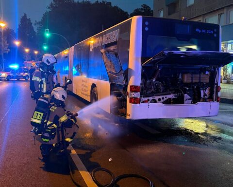 Brennender Bus an Haltestelle, Feuerwehr im Einsatz, Passanten helfen mit Feuerlöscher, Verkehrsbehinderungen.