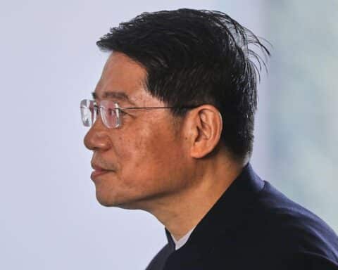 Deng Hongbo spricht, hinter ihm China-Flagge, symbolisiert Handelsfreiheit und internationale Kooperation.