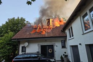 Dachstuhlbrand mit Feuerwehr im Einsatz, Einsatzkräfte löschen flammenden Brand und sichern Gebäude.