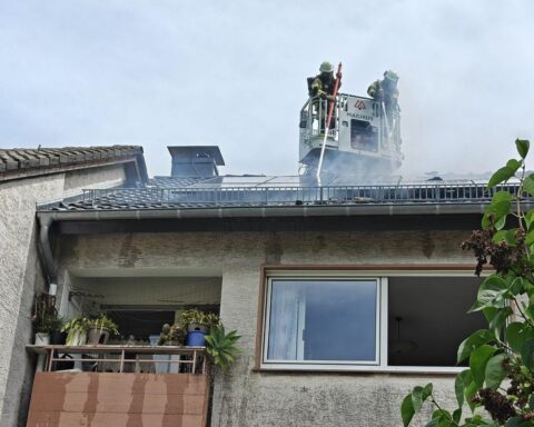 Dachbrand in Wohnhaus: Feuerwehr löscht, Nachbarn helfen evakuieren, starke Rauchentwicklung sichtbar.