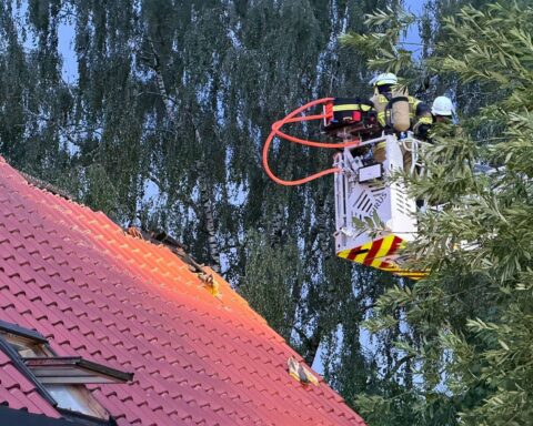 Dachstuhlbrand eines Mehrfamilienhauses nach Blitzeinschlag, Feuerwehr im Einsatz, Rauchentwicklung sichtbar.