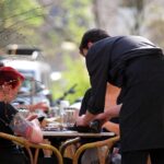 Café-Szene mit Bedienung, symbolisiert die Debatte über Minijobs und Beschäftigungssituation.
