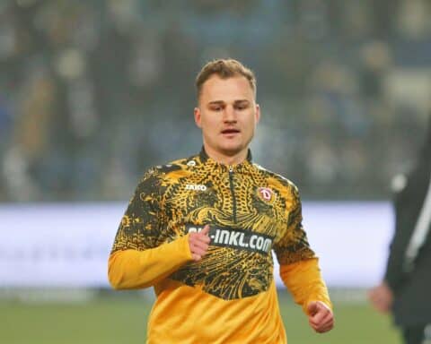 Jakob Lemmer in Dynamo-Dresden-Trikot, jubelnd auf dem Spielfeld, mit Fans im Hintergrund.