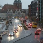 Ein modernes Elektroauto auf einer europäischen Straße mit Flaggen von Großbritannien, Japan und Südkorea.
