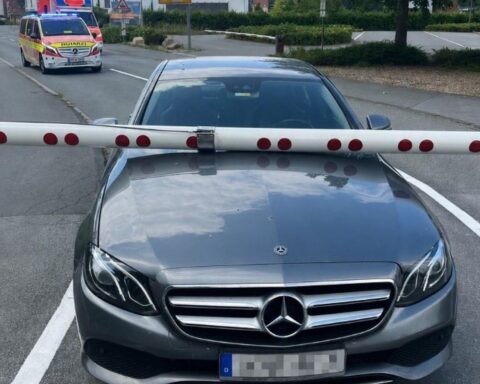 Ein Mercedes am Bahnübergang mit einer geschlossenen Schranke, Polizei im Hintergrund.