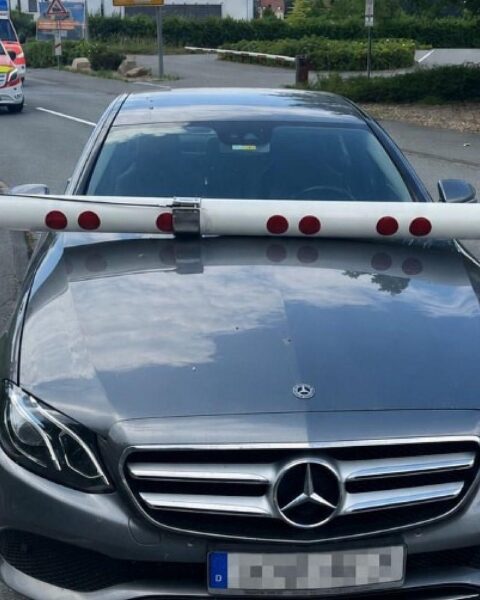 Ein Mercedes am Bahnübergang mit einer geschlossenen Schranke, Polizei im Hintergrund.