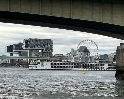 Ein festgefahrenes Fahrgastkabinenschiff auf dem Rhein, Kaimauer im Hintergrund, Polizei vor Ort.