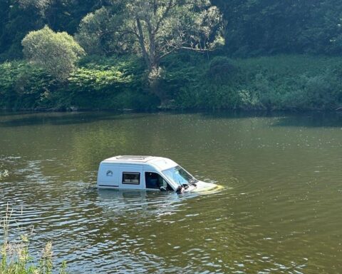 Ein PKW treibt im Wasser des Flusses Sauer, umgeben von Rettungskräften und Traktor.