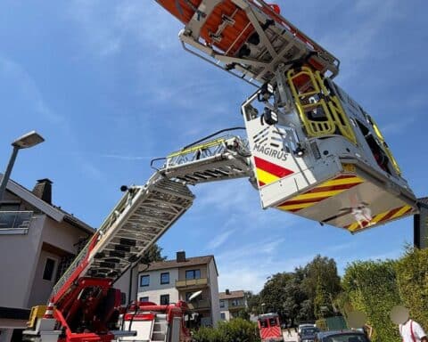 Drehleiter der Feuerwehr rettet verletzte Person aus Dachgeschoss, medizinische Hilfe wird geleistet.