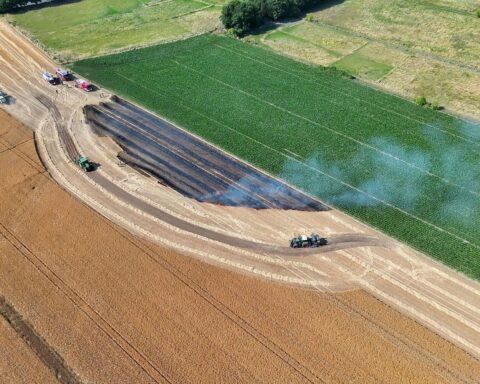 Flächenbrand auf Feld mit Feuerwehr, Traktoren und Drohne unter extremen Bedingungen.