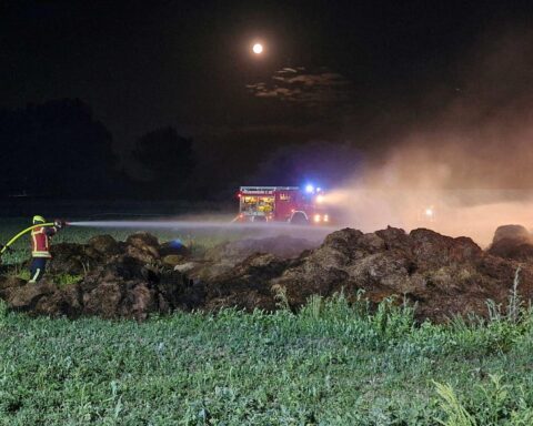 Feuerwehrleute löschen Brand auf landwirtschaftlicher Fläche mit Schläuchen und Traktorunterstützung.