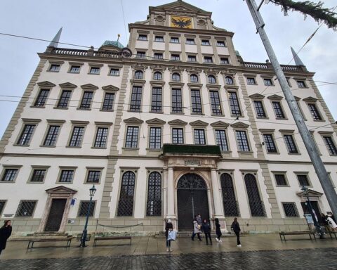 Augsburger Rathaus und Protest gegen Einschnitte bei Fernverkehrsanbindung, symbolisiert durch Züge.