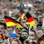 Fußballfans jubeln vor einem Bildschirm, während die WM 2026 diskutiert wird.