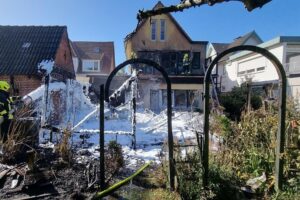 Brandstelle mit Feuerwehr und Rauchentwicklung, beschädigtes Wohnhaus, Einsatzkräfte im Löscheinsatz.
