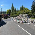Brennender Müllcontainer auf Straße; Feuerwehr löscht Feuer, Fahrer verhindert Fahrzeugschaden.