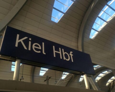 Kieler Hauptbahnhof mit glücklichen Menschen und Wasser im Hintergrund, symbolisiert Lebenszufriedenheit.