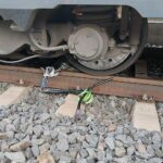 Ein Kinderroller liegt gefährlich auf Bahngleisen, umgeben von Gleisanlagen und Gefahrensymbolen.
