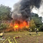 Brennendes Vereinsheim mit dramatischen Flammen und Feuerwehr im Einsatz bei Nacht.