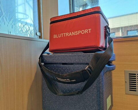 Ein Arzt erklärt Organspende, während Patienten aufmerksam zuhören; Informationskampagne im Vordergrund.