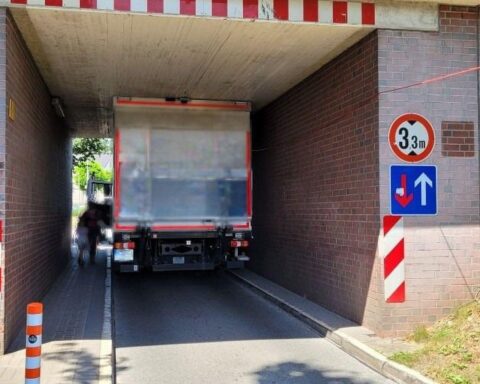 Ein festgefahrener Lkw unter einer Brücke, Polizei und Verkehrssituation beeinträchtigt.