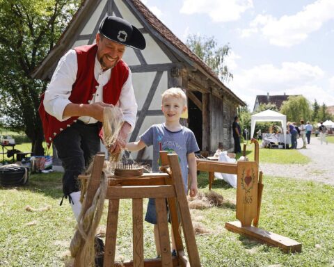 Kinder und Erwachsene erleben traditionelle Flachsverarbeitung in historischen Trachten im Museumsdorf.