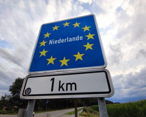 Grenzübergang Deutschland-Niederlande mit Warteschlangen, symbolisiert Konflikt über Grenzkontrollen und Migration.