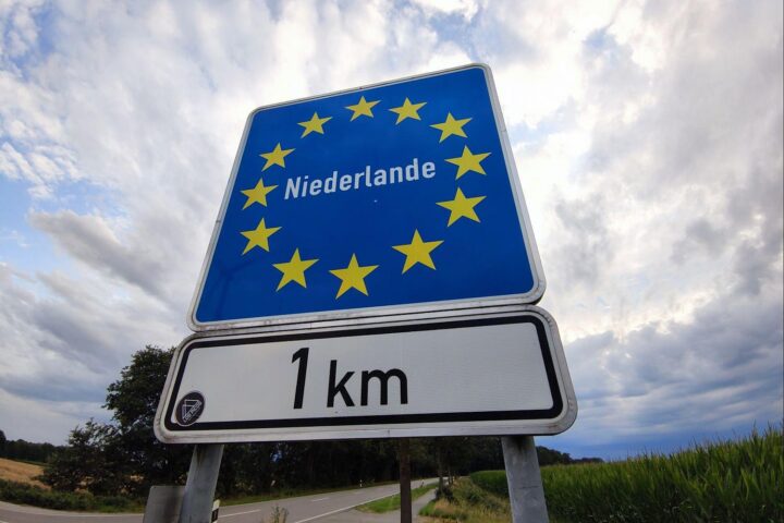 Grenzübergang Deutschland-Niederlande mit Warteschlangen, symbolisiert Konflikt über Grenzkontrollen und Migration.