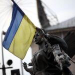 Flagge der Ukraine vor Hintergrund von Zerstörung und Trauer durch die russischen Angriffe.