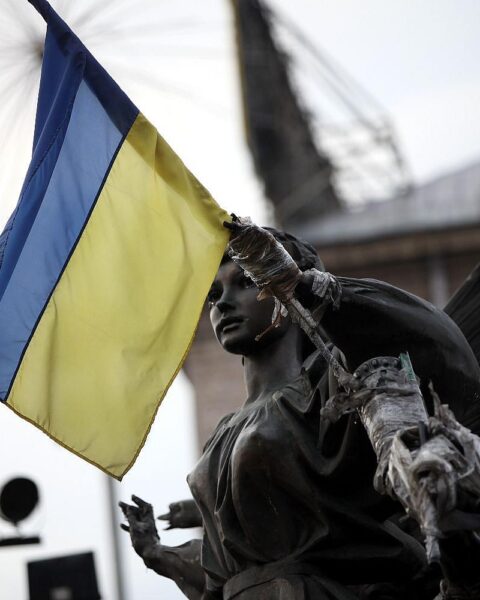 Flagge der Ukraine vor Hintergrund von Zerstörung und Trauer durch die russischen Angriffe.