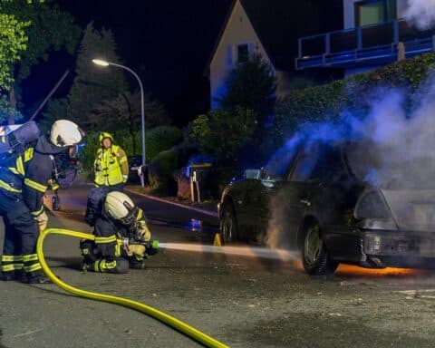 PKW-Brand an der Straße, Feuerwehr löscht Flammen, Rauchentwicklung, nächtlicher Einsatz.