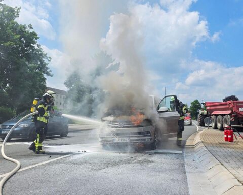 Feuerwehr löscht brennendes Fahrzeug, Unterstützung durch Rettungswagen und Unternehmen. Keine Verletzten.