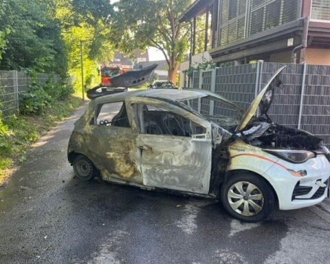 Ausgebrannter Pkw vor Wohn- und Geschäftshaus, Feuerwehr im Einsatz zur Brandbekämpfung.