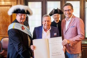 Roland Kaiser trägt sich ins Gästebuch der Stadt Halle ein, umgeben von Fans und Officials.