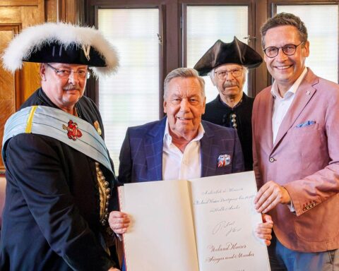 Roland Kaiser trägt sich ins Gästebuch der Stadt Halle ein, umgeben von Fans und Officials.