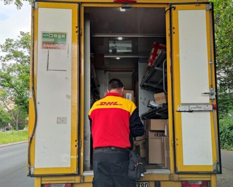 DHL-Paketfahrer mit Paketen, symbolisiert Diskurs über Gewichtsbeschränkung für Paketzustellung.